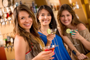 Photo of 3 young women at a bar with martini glasses in hands.